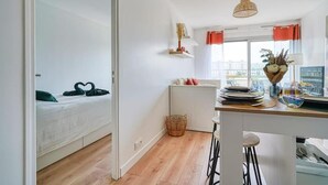 A modern, well-lit room with a bed, a small kitchen area with a dining table, and a view through a window. - ''diamant'' (Choisy-le-Roi)