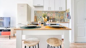 A compact kitchen with a tiled backsplash, white cabinets, and a wooden dining table set for two. - ''diamant'' (Choisy-le-Roi)