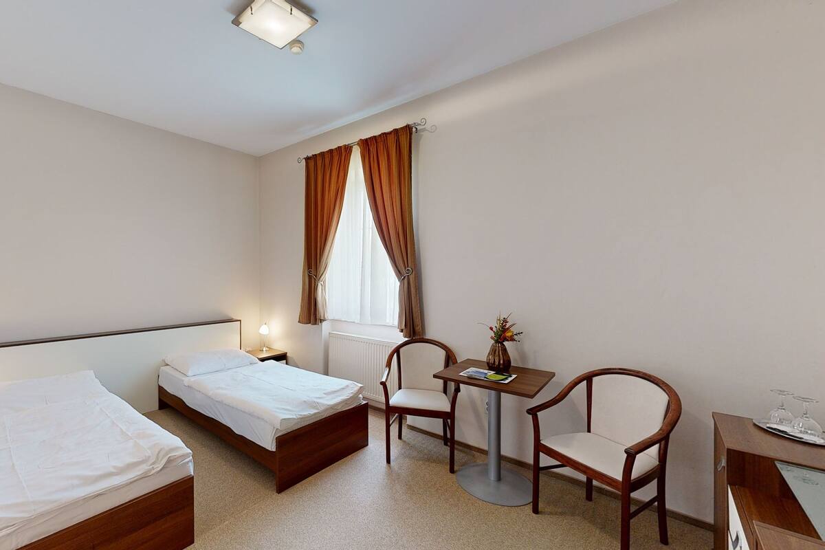 Ett hotellrum med två separata sängar, ett skrivbord med en stol, ett litet bord med en vas och ett fönster med gardiner.