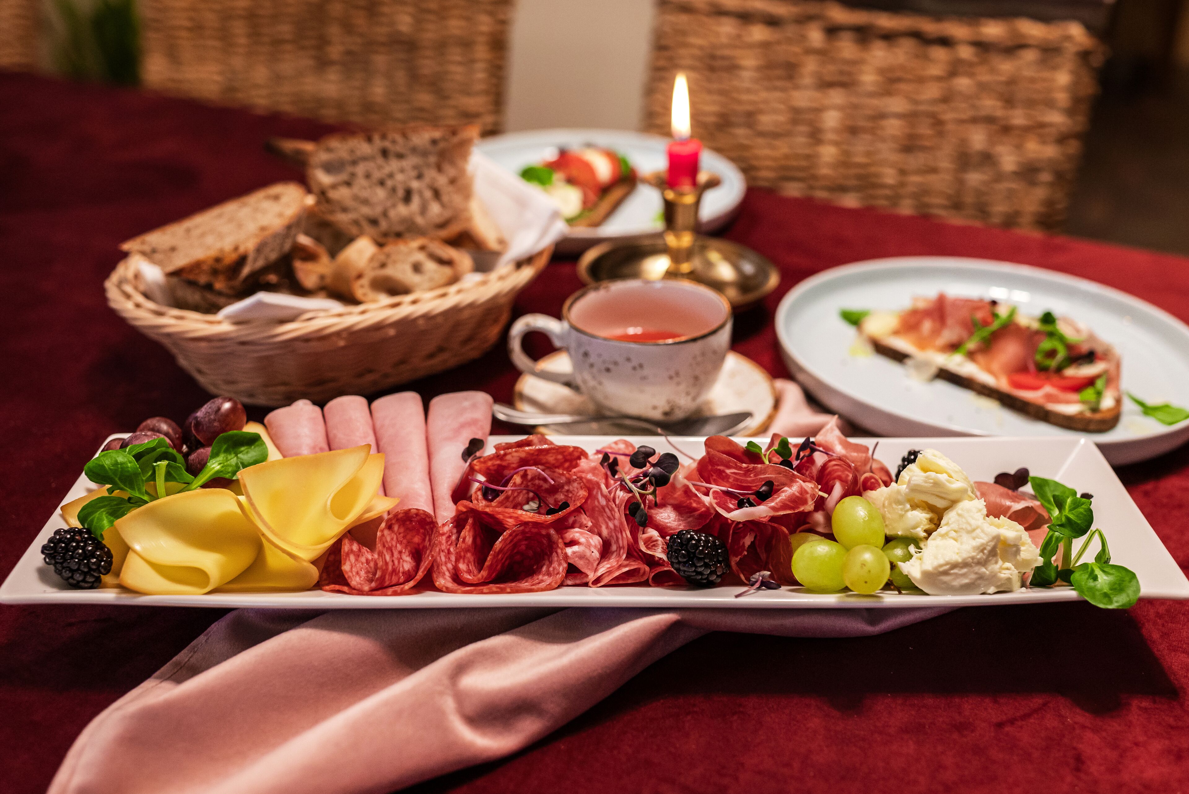 Uma tábua de frios com diversos queijos, carnes e frutas sobre uma mesa.