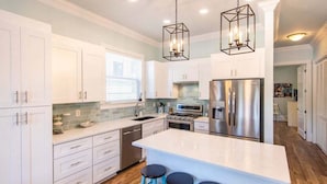 A modern kitchen with white cabinets, a stainless steel refrigerator, and a central island with bar stools. - 3 mins walk to Beach! Guest Beachfront Pool! (Panama City Beach)