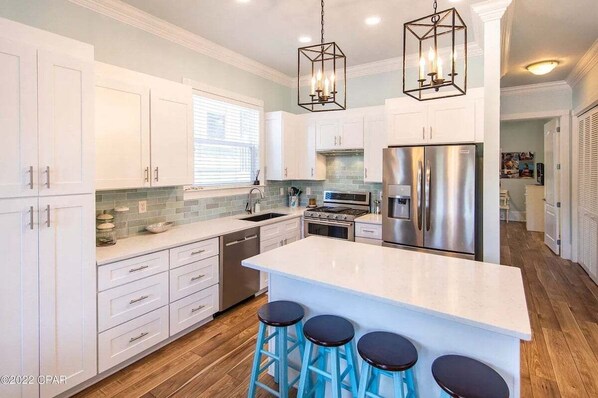 A modern kitchen with white cabinets, a stainless steel refrigerator, and a central island with bar stools. - MAY DISCOUNT! 3 mins from Beach! Guest Beachfront Pool! (Panama City Beach)