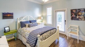 A bedroom with a bed, a nightstand, a chair, a ceiling fan, and a door. - 3 mins walk to Beach! Guest Beachfront Pool! (Panama City Beach)
