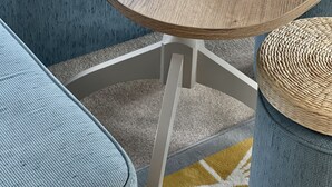 Ein Esstisch ist gedeckt mit Tellern, Gläsern und Besteck, umgeben von einem blauen, gepolsterten Sofa und einem gewebten Korb.