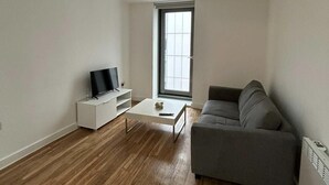 Un salón moderno con un sofá gris, una mesa de centro blanca y un televisor sobre un mueble blanco.