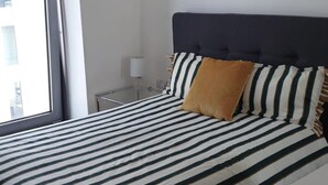 Un dormitorio con cama, mesita de noche, lámpara y ventana.