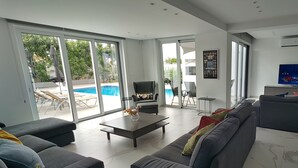 A spacious living room with a grey sofa, a coffee table, and a pool view through large sliding glass doors.