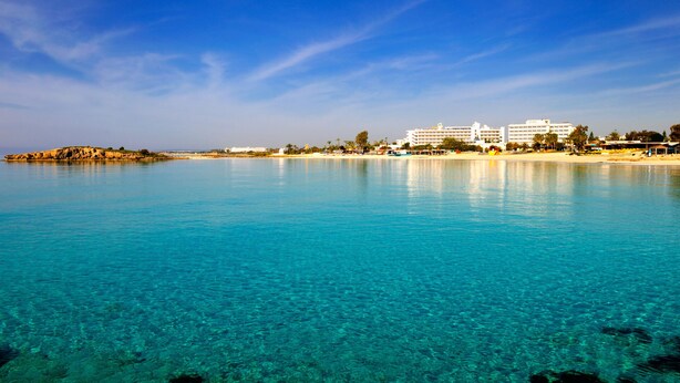 A coastal hotel with clear blue waters, beachfront, and multiple white buildings.
