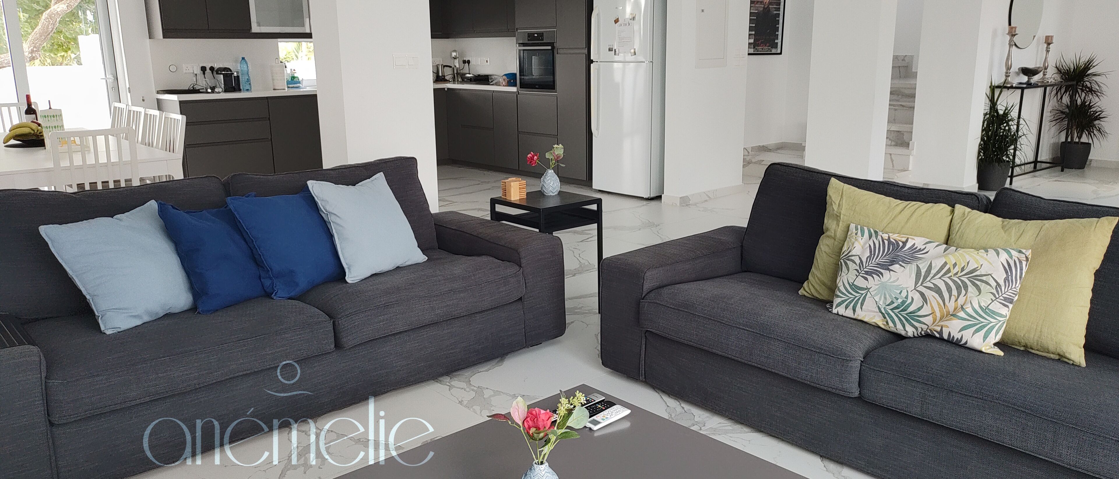 A modern living room with two grey sofas, a coffee table, and a kitchen in the background.