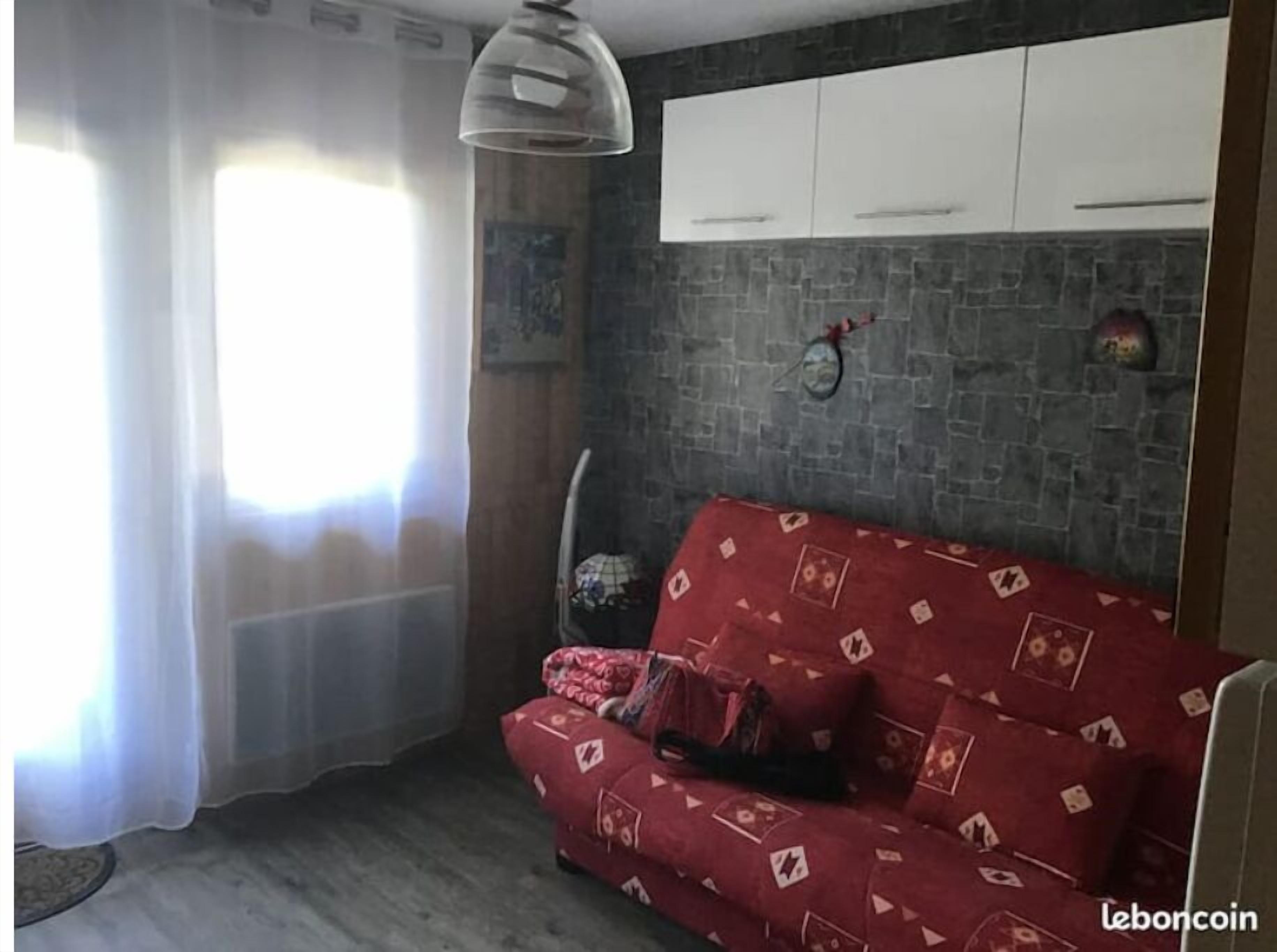 Een woonkamer met een rode bank, een gebreid plaid, een hanglamp en een stenen muur.