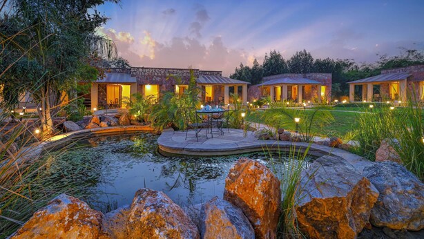 A resort with stone buildings, a pond, and outdoor seating areas.