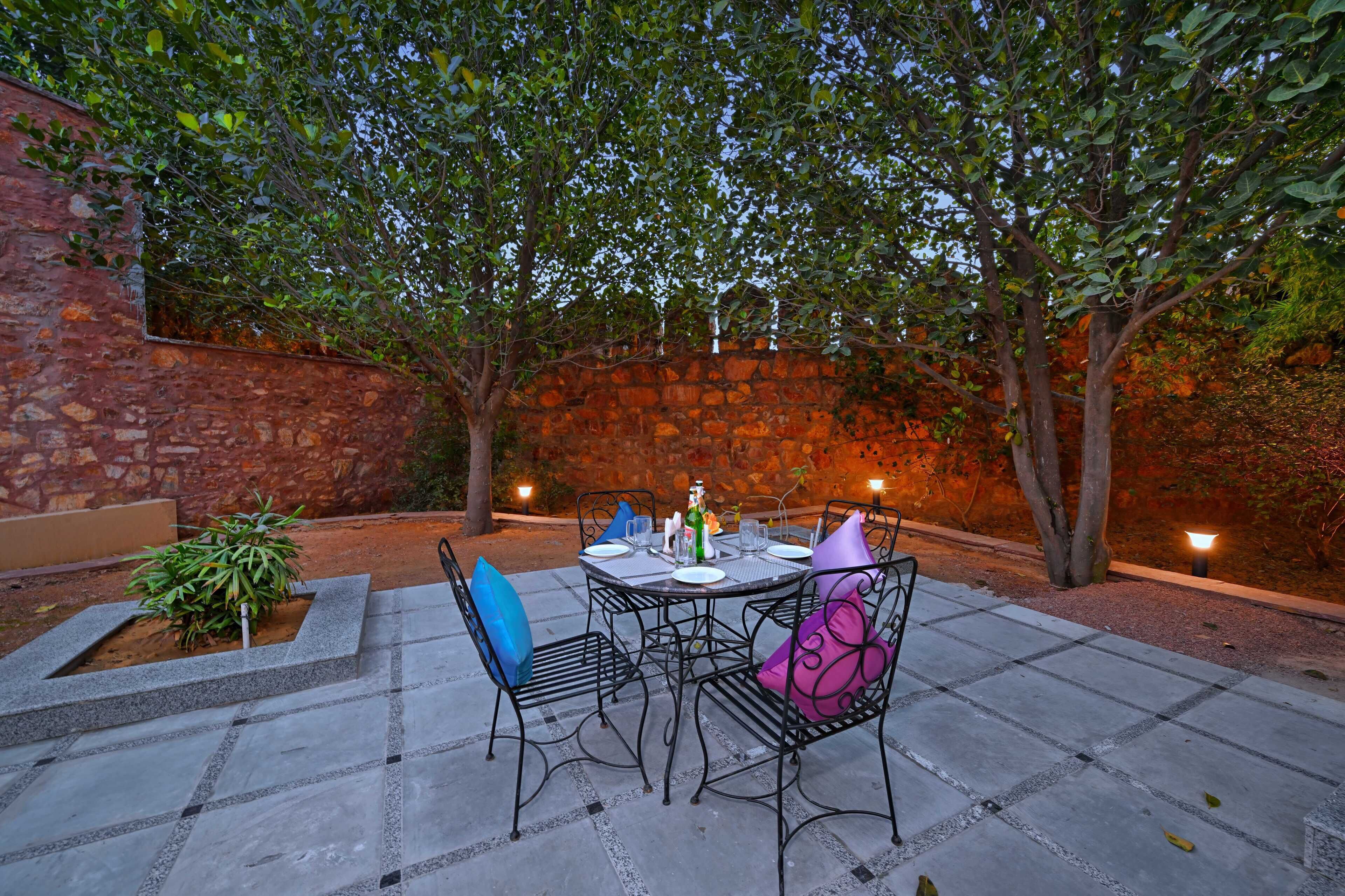An outdoor patio with a stone wall, a table set for dining, and chairs with cushions.