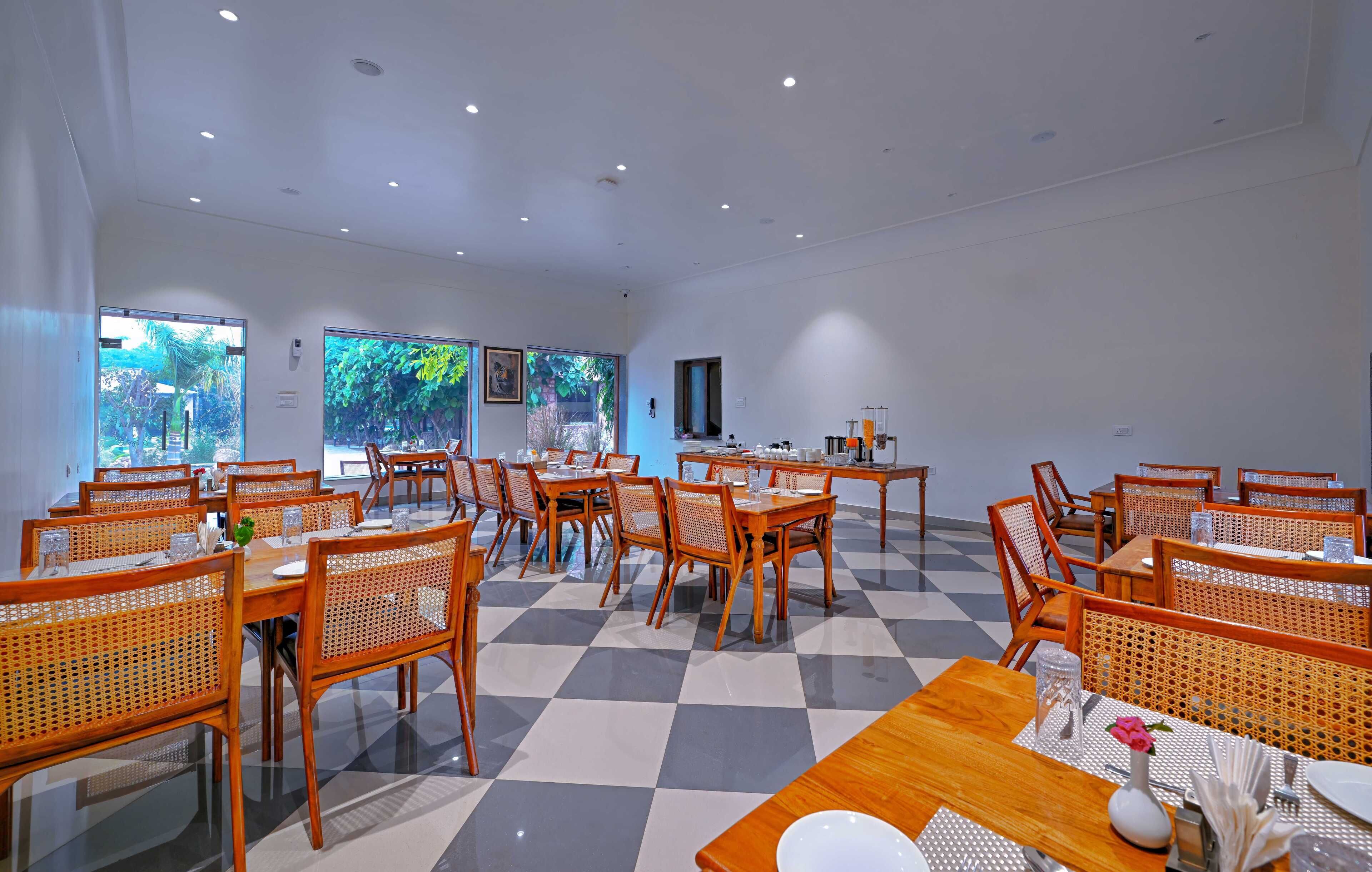 Un vaste espace dédié à la salle à manger, doté d’un sol à carreaux, de tables et de chaises en bois, et de grandes fenêtres offrant une vue sur la verdure.