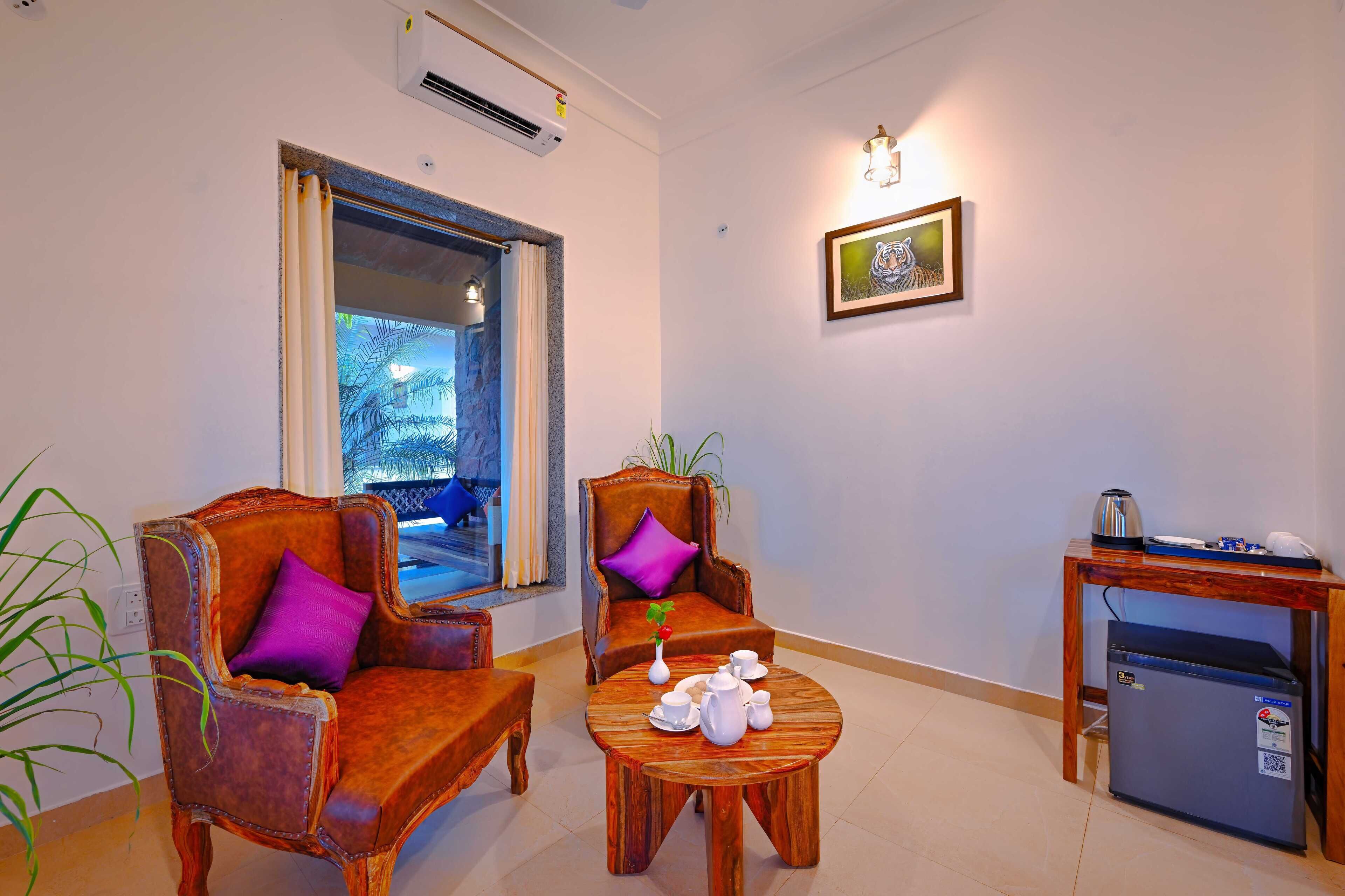 A room with two leather armchairs, a wooden coffee table with tea set, a small table with a kettle, and a refrigerator.