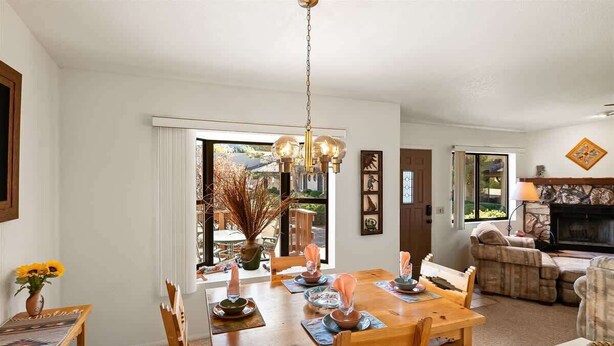 Un coin repas avec une table en bois dressée pour quatre personnes, un lustre et une vue sur l’extérieur.