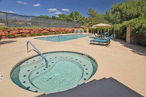 Une piscine dotée de chaises longues et d’un jacuzzi, entourée de rochers et de verdure.