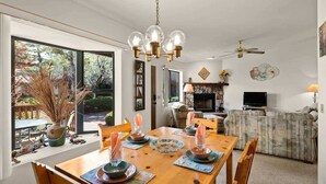 Un coin repas avec une table en bois dressée pour quatre personnes, un lustre et une cheminée en arrière-plan.