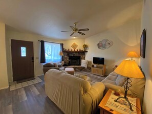 A living room with a fireplace, a ceiling fan, a television, and a lamp.