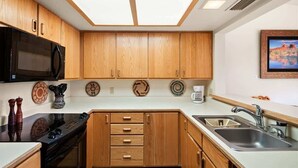 Une cuisine de taille réduite, dotée de meubles en bois, d’un micro-ondes noir, d’une cuisinière et d’un évier.