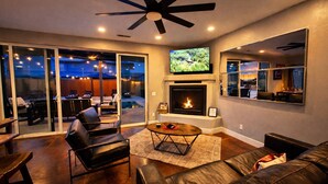 A living room with a fireplace, leather furniture, a ceiling fan, and a TV mounted on the wall. - Desert Hideaway: 3-Bedroom Home with Year-Round Private Pool & Hot Tub (Moab)