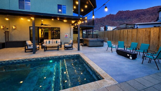 A residential backyard with a swimming pool, outdoor seating, and string lights. - Desert Hideaway: 3-Bedroom Home with Year-Round Private Pool & Hot Tub (Moab)