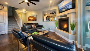 A modern living room with a fireplace, leather furniture, a ceiling fan, and a large TV. - Exclusive Retreats Desert Hideaway 3 Bedroom all Suite home with Private pool #2 (Moab)