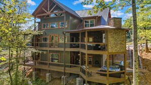 Eine mehrstöckige Blockhütte mit einem Steinkamin, mehreren Balkonen und einer Whirlpoolanlage auf der unteren Terrasse.
