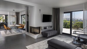Una sala de estar moderna con chimenea, comedor y un amplio ventanal con vista a la ciudad.