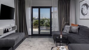 Una sala de estar moderna con un sofá gris, un televisor de pantalla plana, una mesa de centro y vista a un puerto deportivo a través de amplias puertas de vidrio.