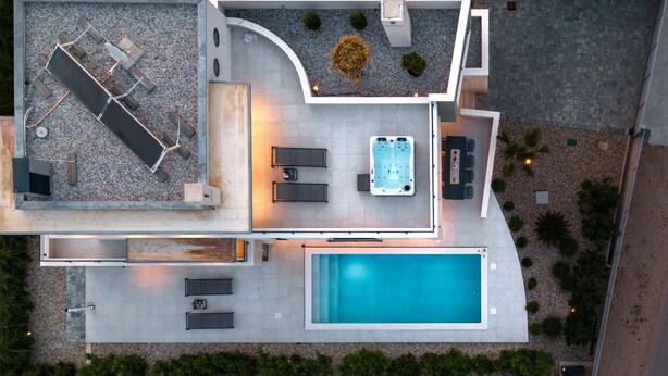 Vista aérea de una casa moderna con piscina, mobiliario exterior y bañera de hidromasaje.