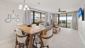 Un vaste espace de vie comprenant une table à manger en bois, des chaises blanches, un canapé et un ventilateur de plafond.