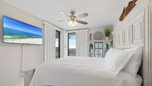 Une chambre avec un grand lit, un ventilateur de plafond, une télévision et une vue sur la plage.