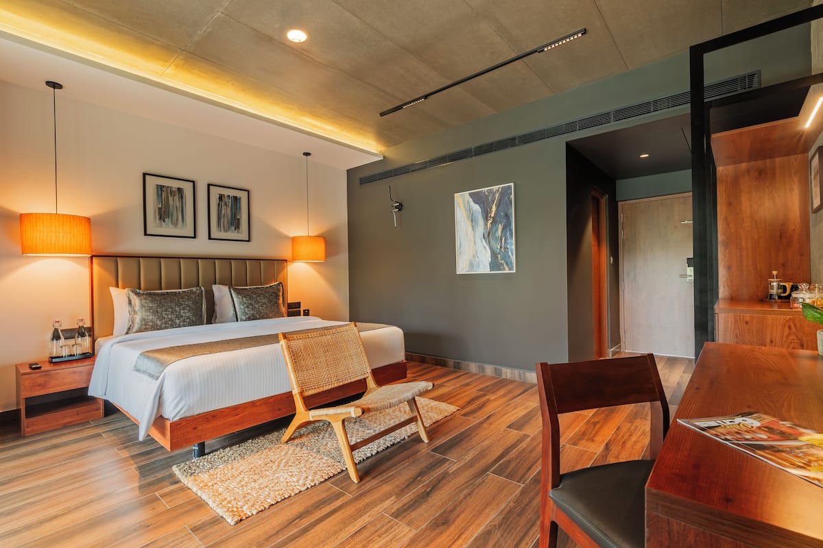 A modern bedroom with a large bed, two bedside lamps, a wooden headboard, and a dining table with chairs.