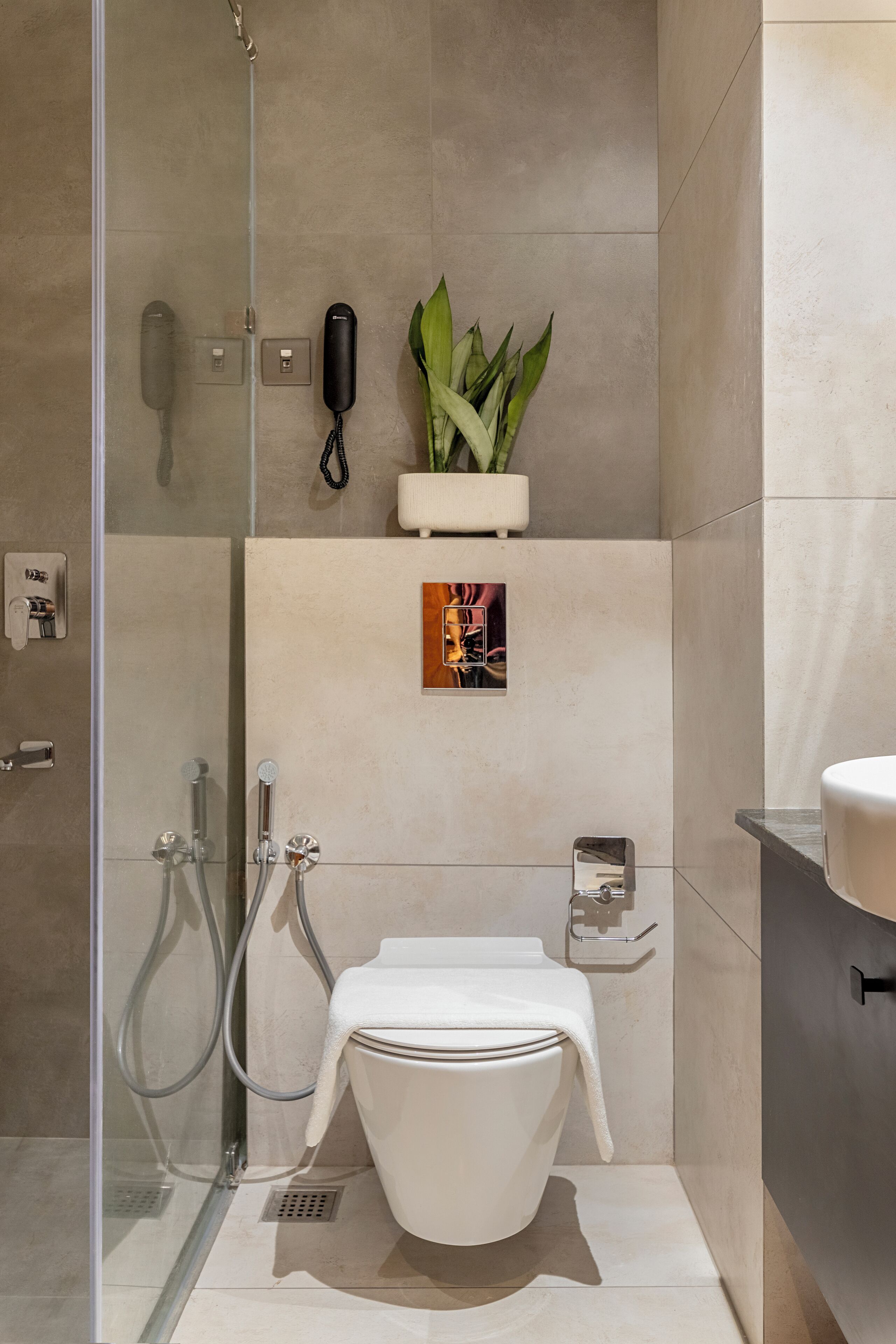 Un baño moderno con cabina de ducha de vidrio, inodoro, lavamanos y una planta en maceta.