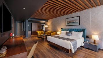 Quarto de hotel moderno com uma cama grande, teto de madeira, televisão, escrivaninha com cadeira e uma pequena mesa com cadeiras.