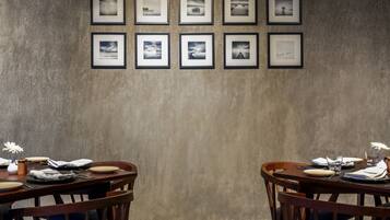 A dining area with a table set for two, framed pictures on the wall, and a textured wall.