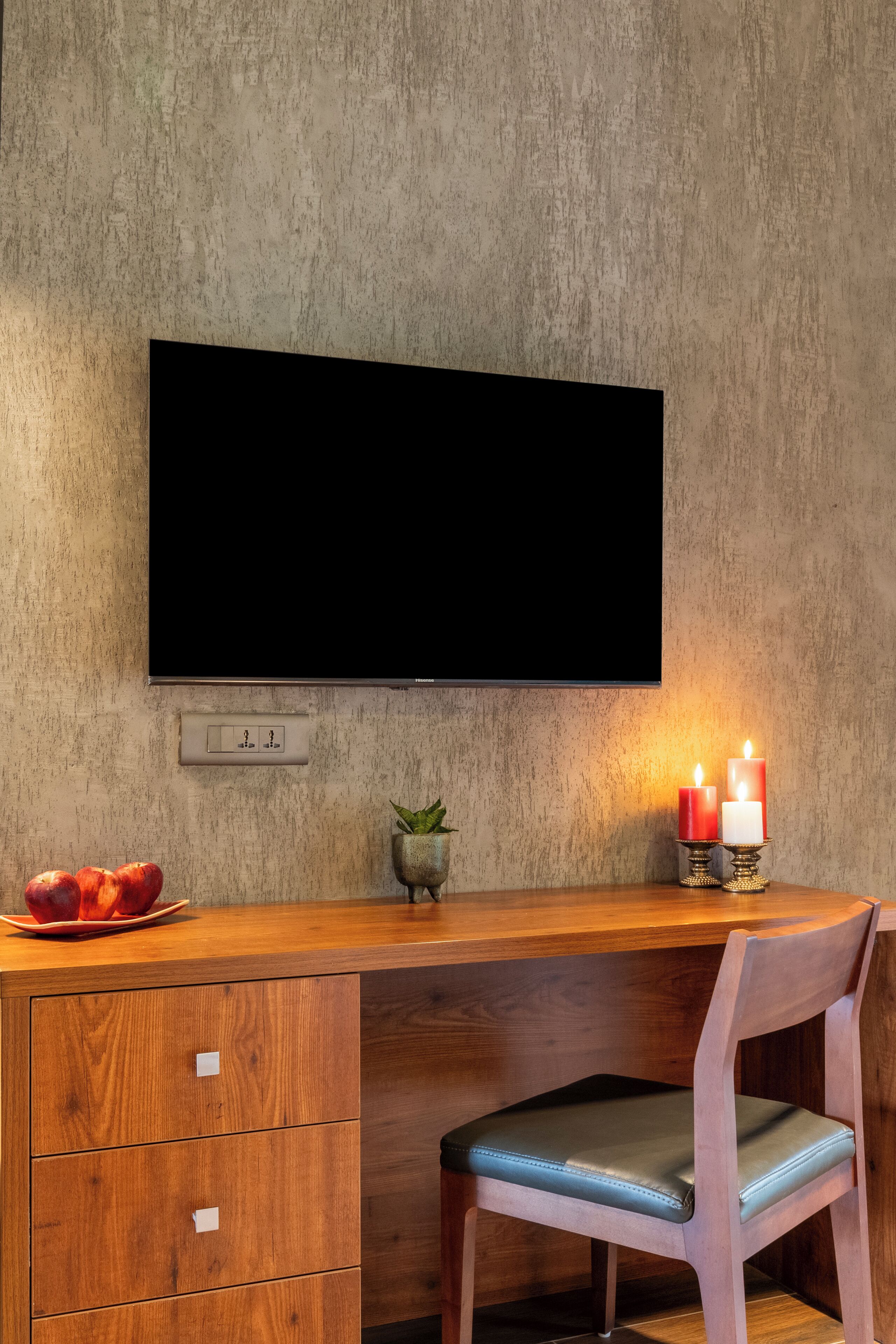 A modern room with a wooden desk, a chair, a television mounted on the wall, and a small potted plant.