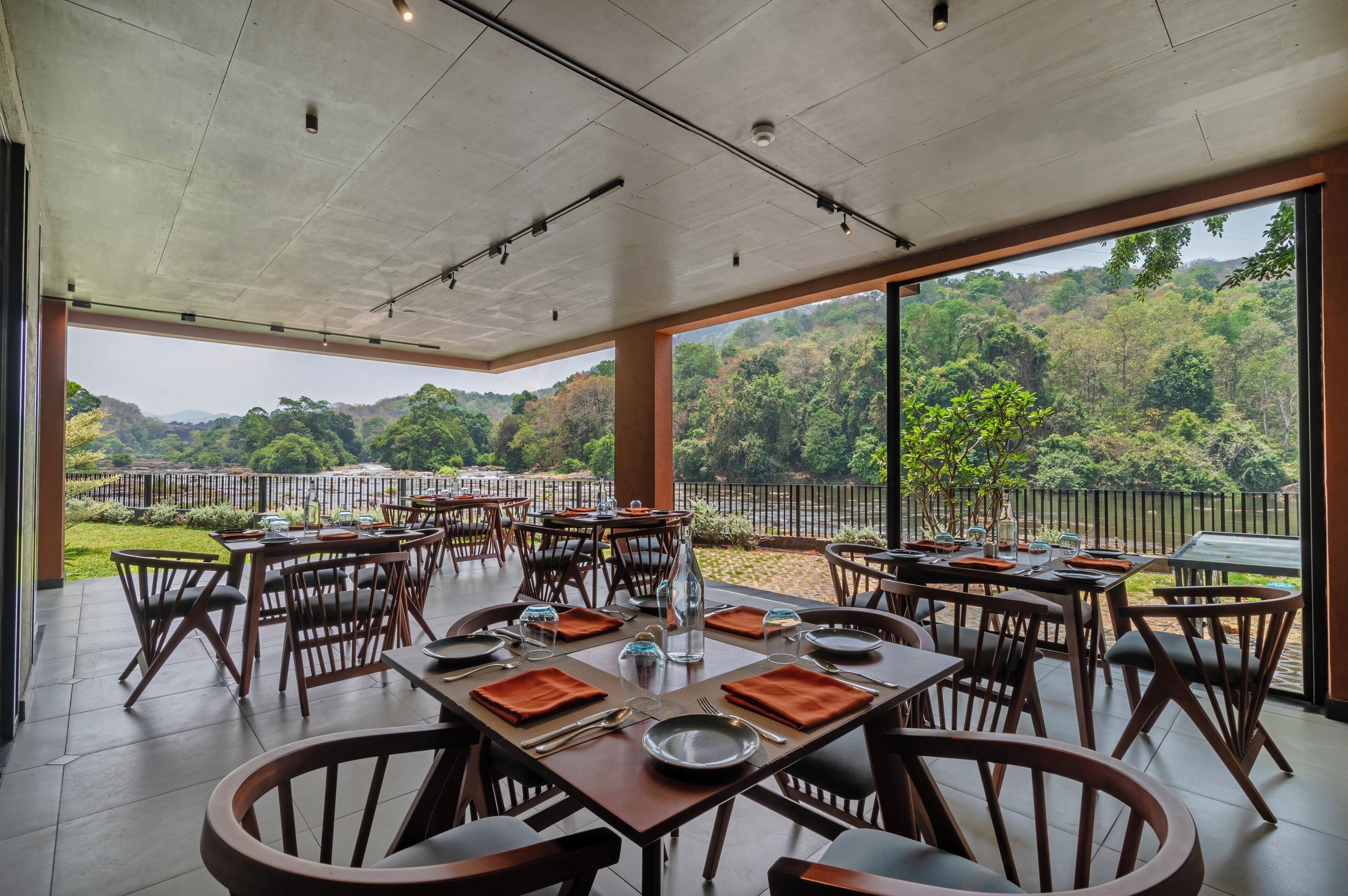 Un ristorante con posti a sedere all'aperto, tavoli apparecchiati con piatti e posate, e vista su un paesaggio boschivo.