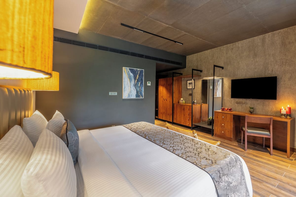 A modern hotel room with a large bed, a wooden desk, a flat-screen TV, and a wardrobe.