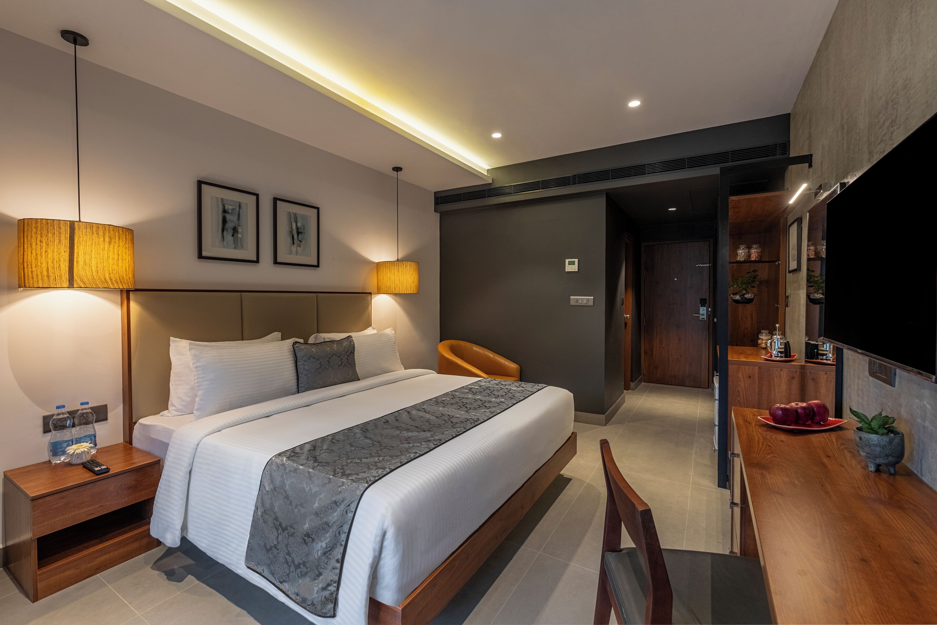 Una habitación de hotel moderna con una cama grande, lámparas de noche, una mesita de noche de madera, un escritorio con silla y un televisor.