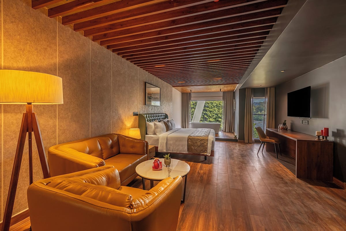 A modern hotel room with a wooden ceiling, a sofa, a bed, a desk, and a TV.