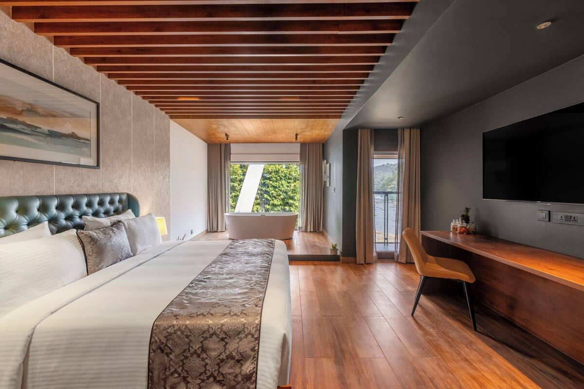 A modern hotel room with a large bed, a bathtub, a desk, and a TV.