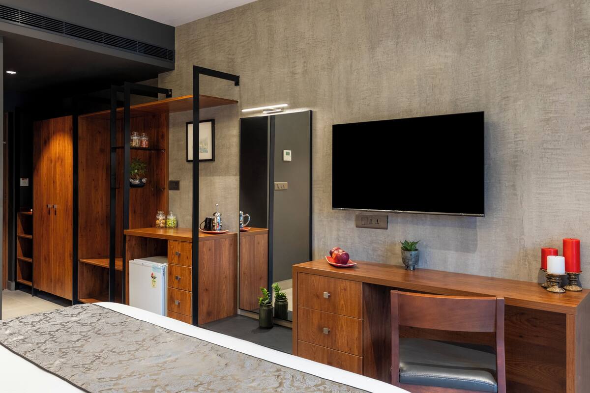 A modern kitchen with wooden cabinets, a built-in refrigerator, a flat-screen TV mounted on the wall, and a small dining area with a wooden table and chair.
