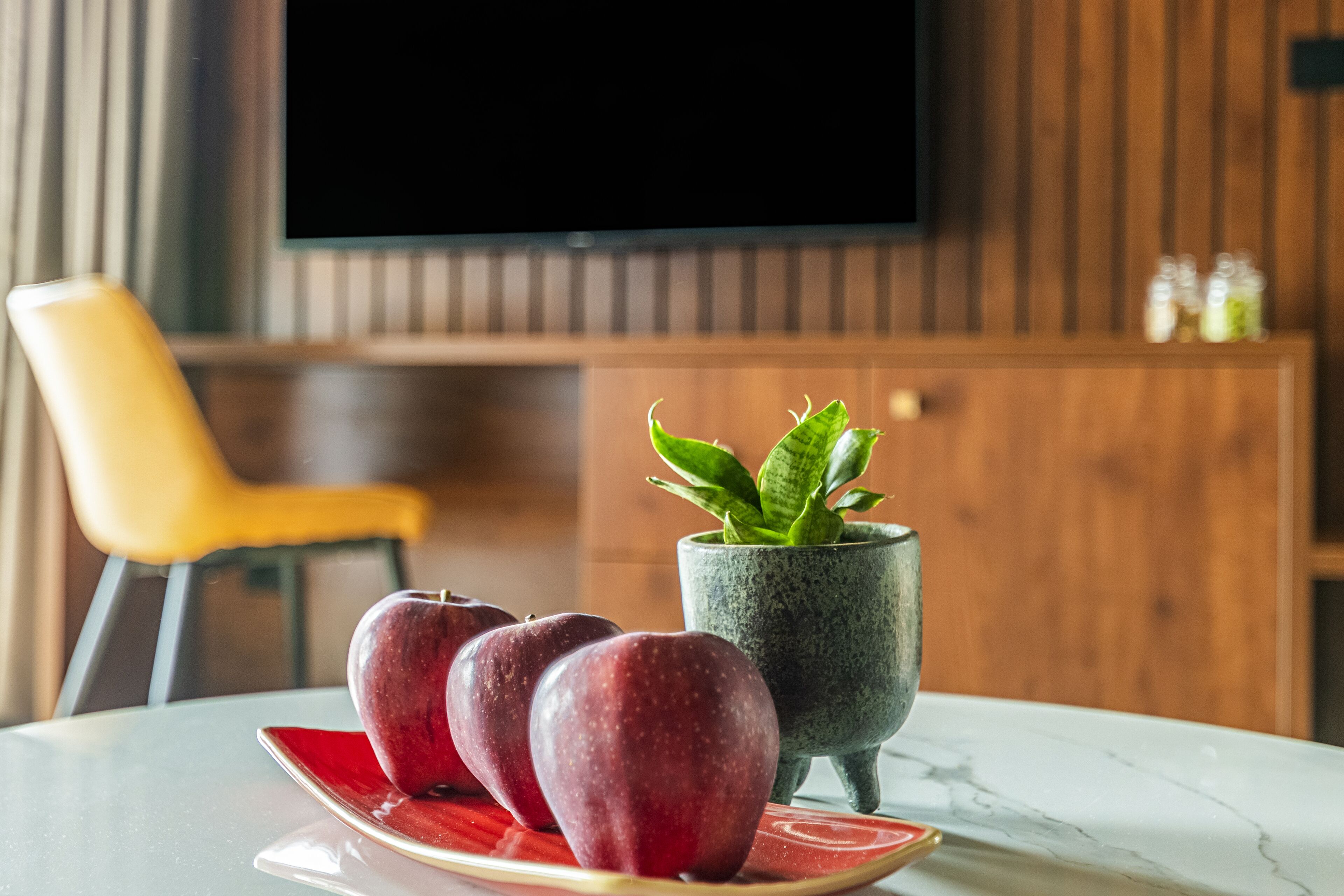 Una mesa con un plato de manzanas rojas y una planta en maceta.