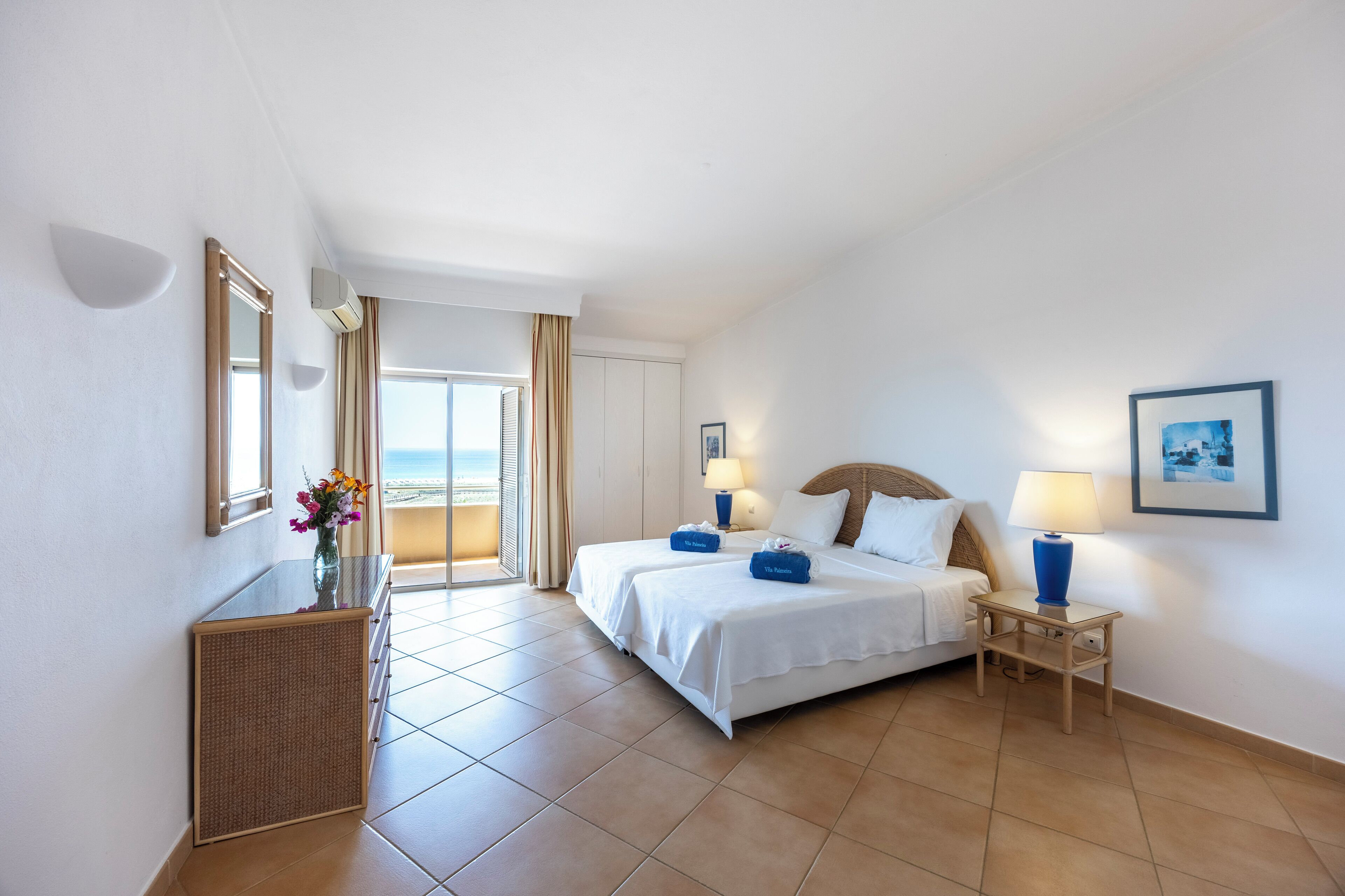 Habitació d'hotel amb un llit, taules de nit, escriptori i vista al mar.