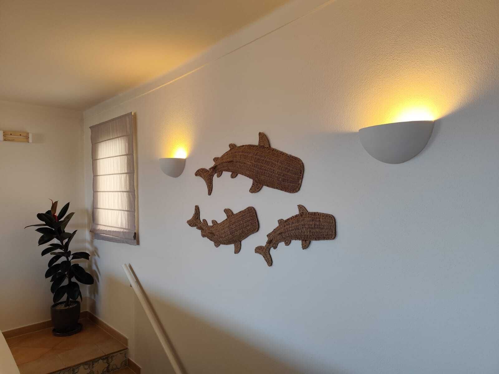 Un couloir avec une plante en pot, une fenêtre avec des stores et des appliques murales fixées au mur, chacune équipée d'une ampoule.