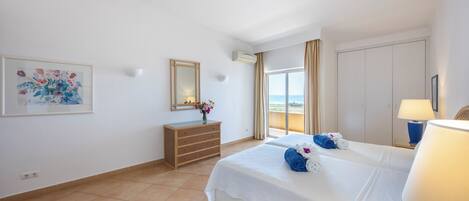 A hotel room with a bed, a dresser, a mirror, a painting, and a view of the sea.