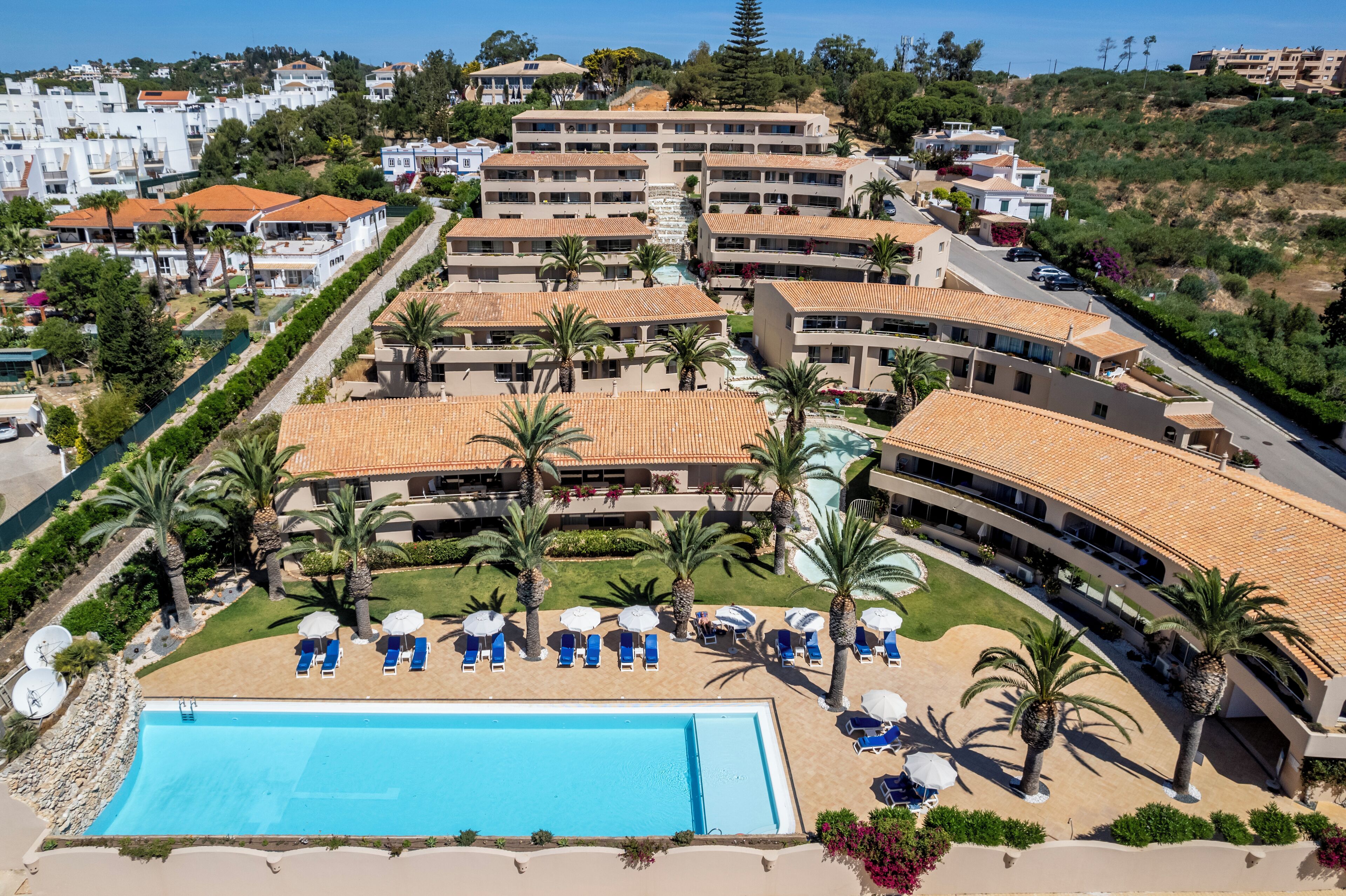 A resort with multiple buildings, a swimming pool, and palm trees.