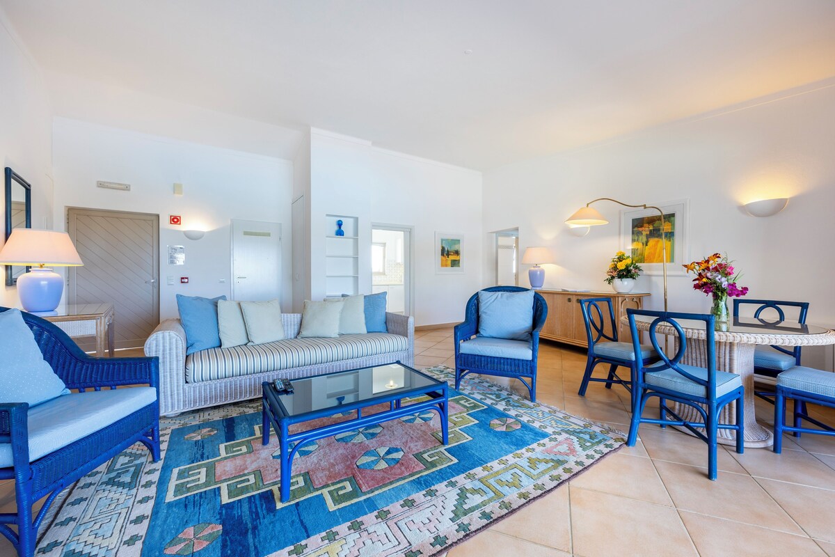 A modern living room with a sofa, armchairs, a coffee table, and a dining area with chairs and a table.