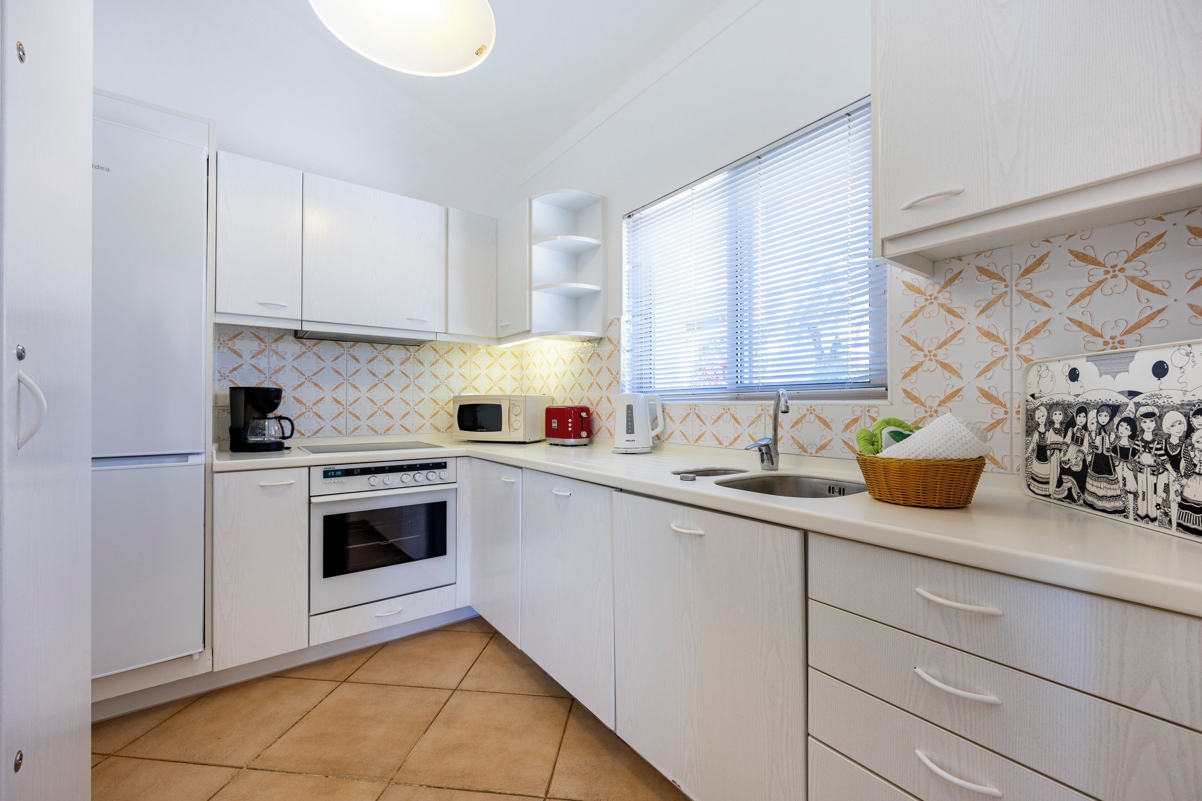 Una cocina compacta con armarios blancos, microondas, tostadora y pileta.
